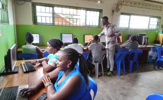 Women and youth learning to use computers, being instructed by a librarian, in a library.