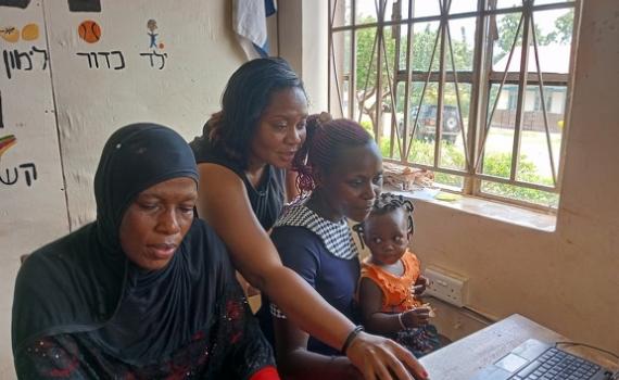 Women learning to use computers at a previous ICT camp in Uganda. One of the women has a baby on her lap.