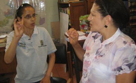 Maria Eugenia, right, practises sign language with a librarian. A library trainee practises sign language with a librarian.